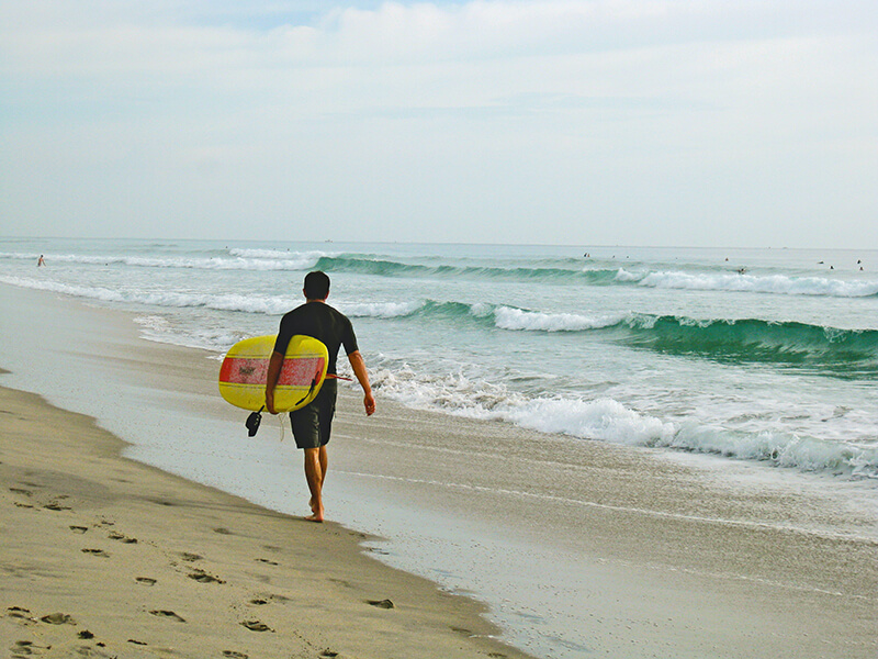 Man holding a surf board walking down a beach.
