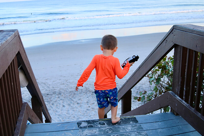 A young boy holding a toy car as he walks down stairs at the beach