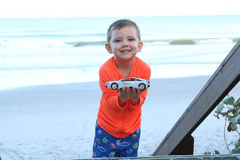 Young boy holding an EV toy car at the beach